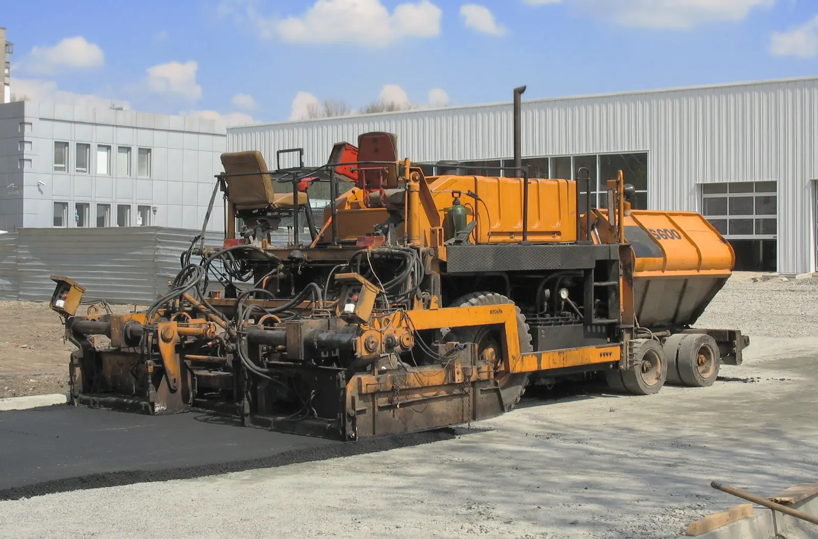 Orange asphalt paving machine parked on a paved yard beside a building