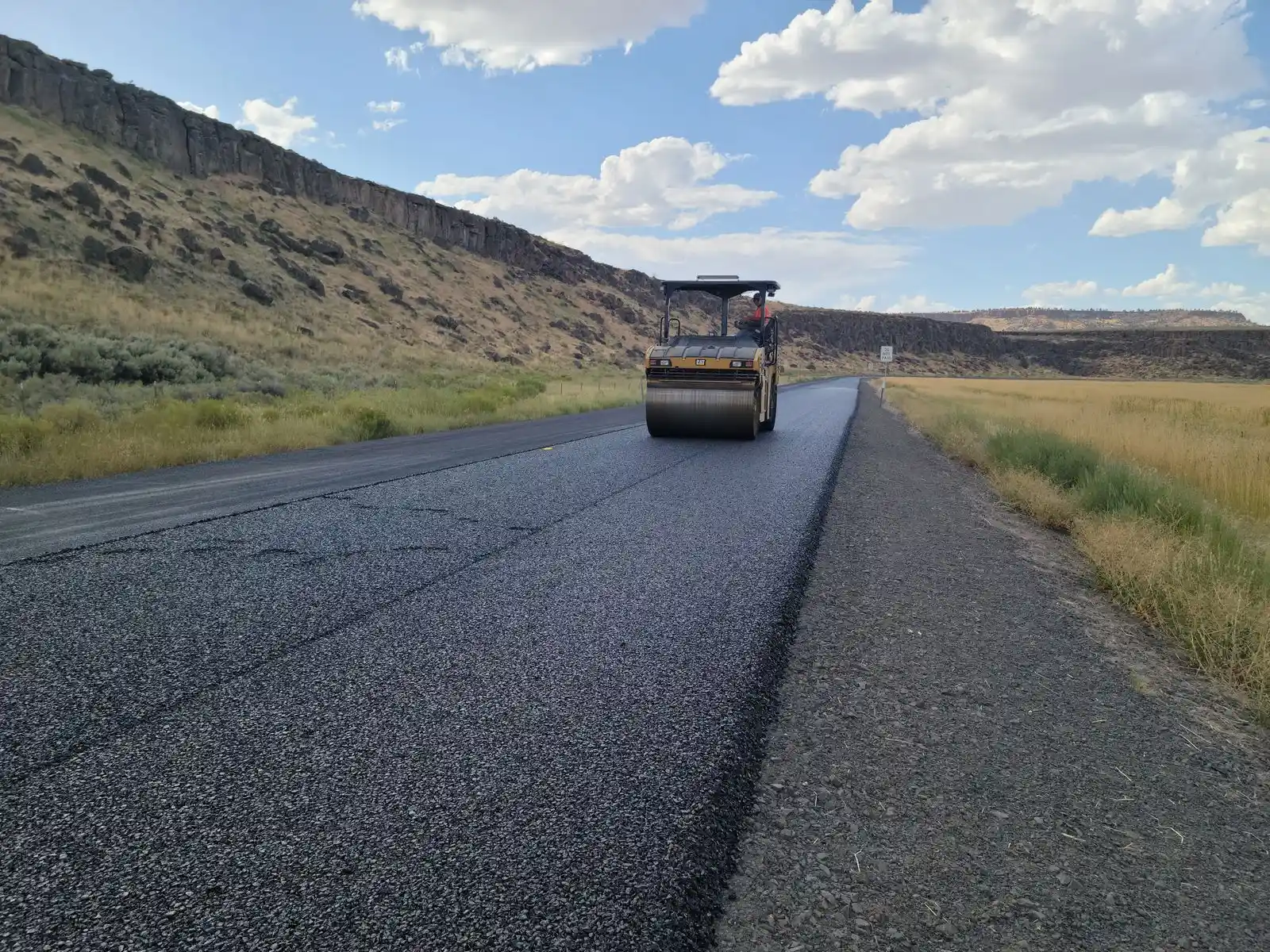 Road roller compacting a fresh layer of hot mix asphalt under a blue sky