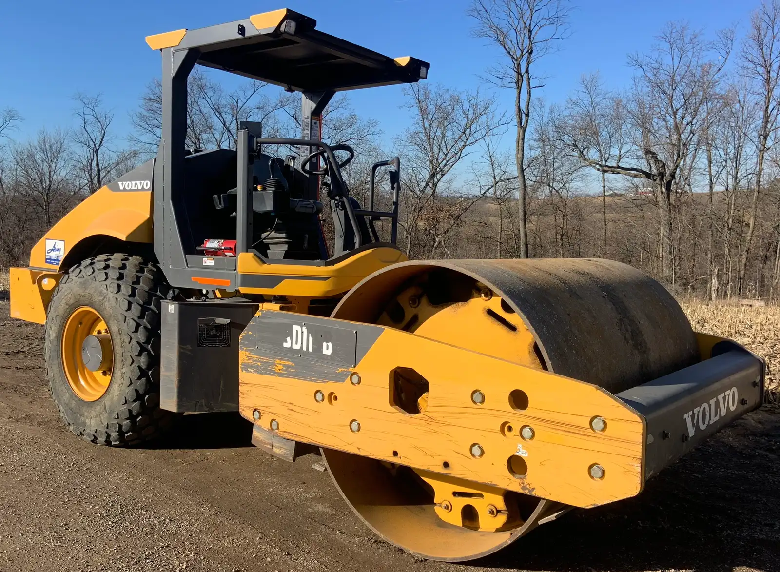 Yellow smooth-drum compactor parked on a graded gravel base before paving